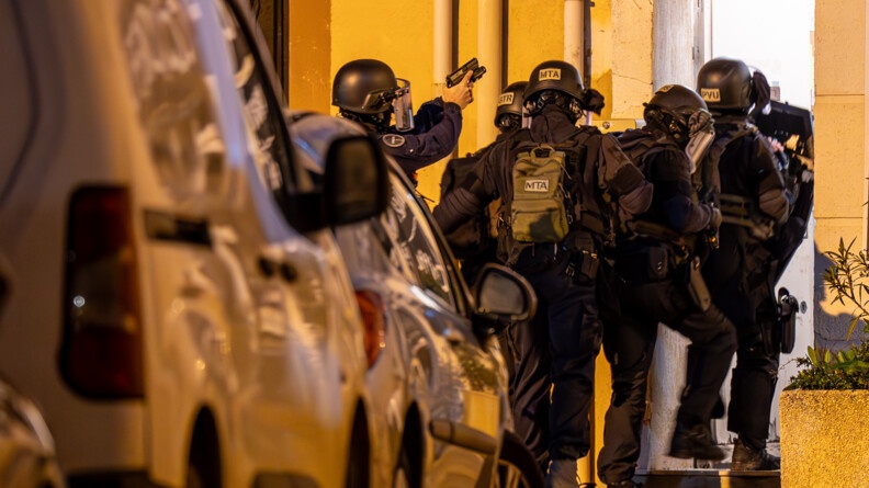 Devant des voitures stationnées, conq gendarmes équipés de casques et de gilets lourds s'engagent dans une porte