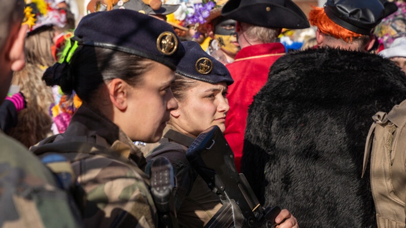 La photo repr&eacute;sente deux femmes gendarmes, portant la tenue kakie, dans la rue, aux c&ocirc;t&eacute;s des carnavaleux, qui portent un d&eacute;guisement, lors du carnaval de Bergues.
