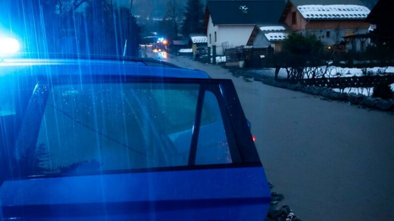 A la nuit tombante, un véhicule gendarmerie, vu de trois-quarts avant, portière avant ouverte et gyrophare allumé, stationné en bordure d'un chemin inondé au milieu des habitations.