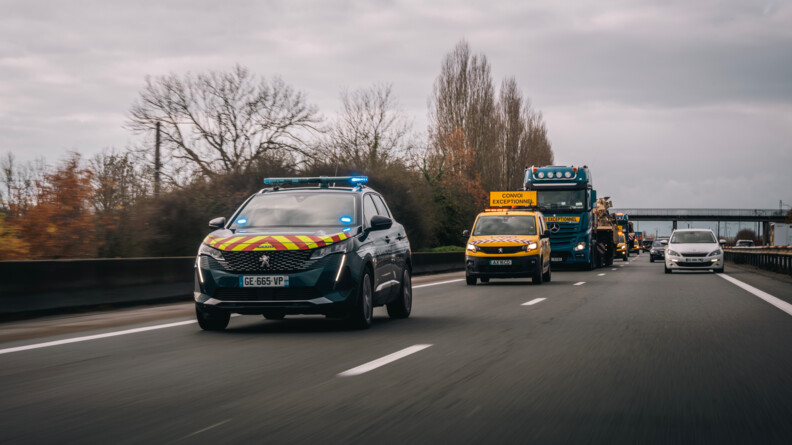 Photo de plus proche du convoi passant sur l'autoroute avec en premier plan une voiture gendarmerie ouvrant le convoi.