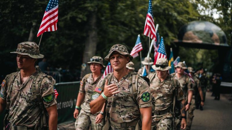 Agrandir l'image Un groupe de militaires, en treillis kaki, marchent ensemble, face à l'objectif. Plusiers d'entre eux portent un drapeau américain, accroché à leur sac à dos.