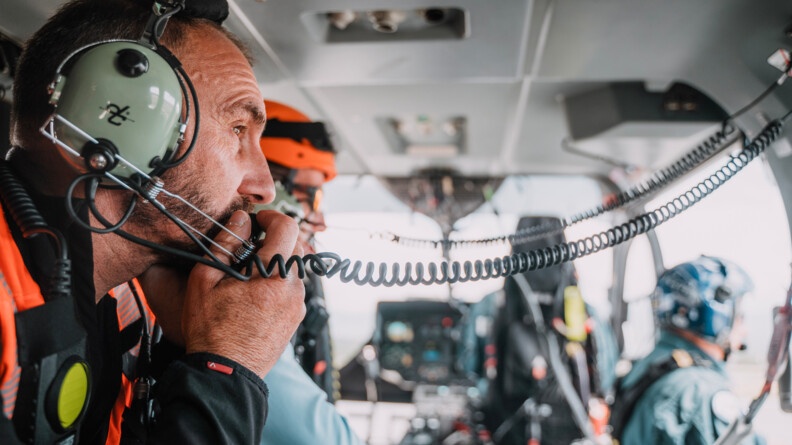 Vue dans un cockpit d'hélicoptère, un gendarme de profil tête nue, tient son micro près de sa bouche