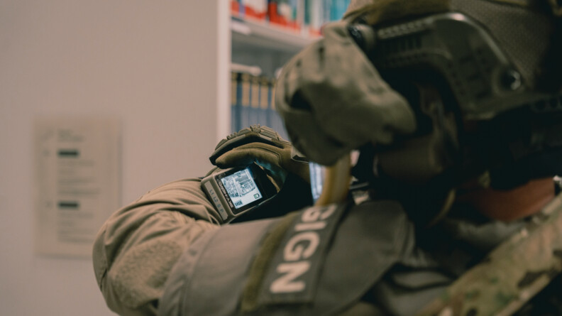 Au premier plan, de dos, un équipier de la force intervention du GIGN en train de regarder un écran vidéo fixé à son poignet gauche.
