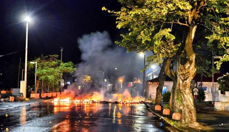 Image d'une chauss&eacute;e en feu, sur un large axe de circulation urbaine. Le feu prend toute la largeur de la voie, et il s'en d&eacute;gage une fum&eacute;e blanche. Il fait nuit.