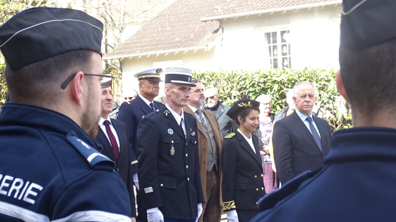 Deux gendarmes vus de dos au garde-à-vous. Face à eux, les autorités civiles et militaires au garde-à-vous.