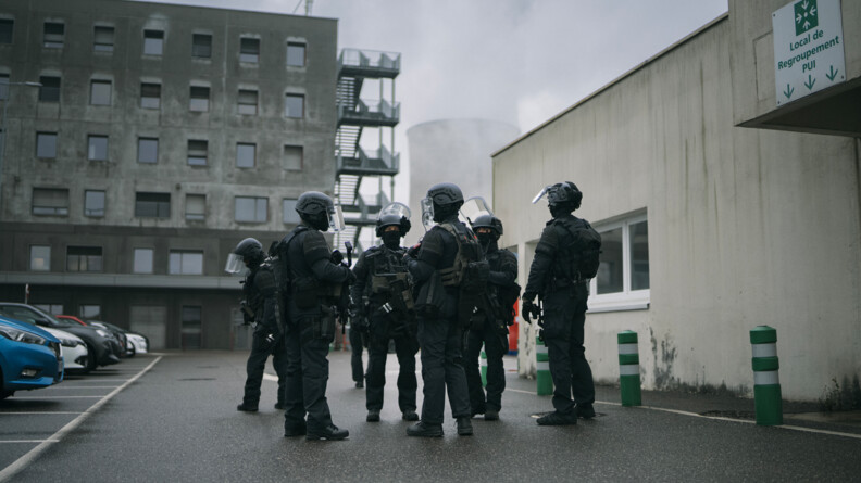 En extérieur devant la centrale, les gendarmes échangent avant le lancement de l'exercice. Ils sont en tenue d'intervention avec un casque et des protections.
