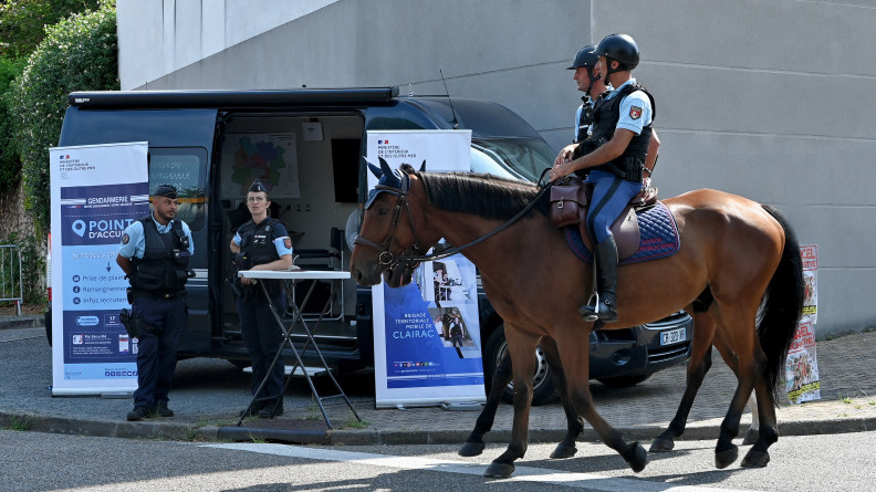 Deux gendarmes de la Garde républicaine patrouillent côte à côte, à cheval, à l'occasion du festival Garorock. derrière eux se trouve un véhicuyle de la gendarmerie, ainsi que deux gendarmes, debout devant un kakémono portant l'inscription "Point d'accueil"
