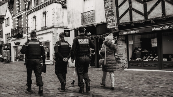 2 gendarmes et un policier de dos ainsi qu'une femme, marchant dans une rue pavée.