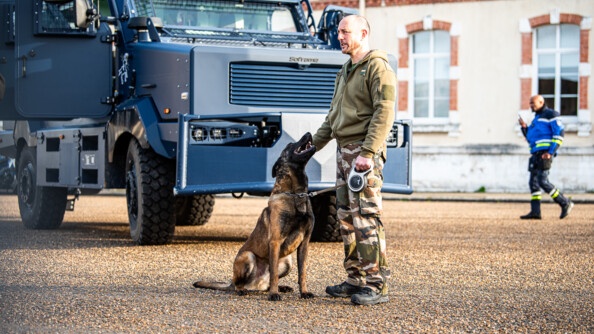 Equipe cynophile, composée d'un chien et de son maître, devant un véhicule blindé Centaure.