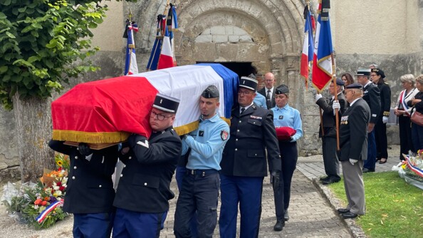 Porté par quatre gendarmes, un cercueil recouvert d'un drapeau français frangé d'or, à la sortie d'une église. de part et d'autres, des militaires, civils et autorités