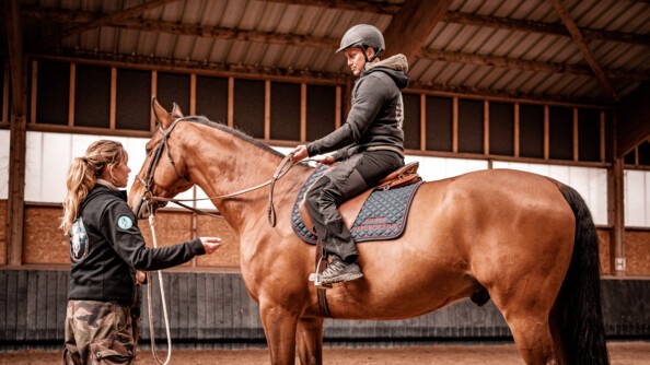 Nicolas, à droite, participant au stage Cent'Or, sur son cheval, échange avec son accompagnante, debout à gauche, dans le manège.