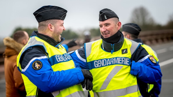 Photo de deux réservistes de la gestion des flux entrain de rigoler ensemble. Dans le fond on aperçoit un civil discuter avec d'autres gendarmes.