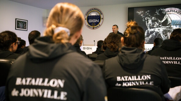 Des sportifs de dos au sweat noir floqué en blanc "bataillon de Joinville" écoute le chef du GIGN qui s'adresse à eux