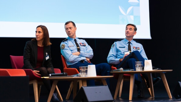 Photo de trois intervenants au colloque, assis sur des chaises rouges sur l'estrade d'un amphi.