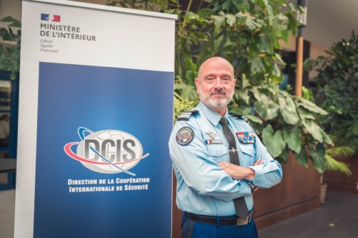 Un colonel de gendarmerie en tenue, les bras croisés devant un panneau DCIS