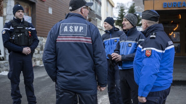 De part et d'autre d'un ASVP de dos, quatre gendarmes, devant les bâtiments au croisement d'une rue