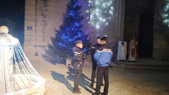 Trois gendarmes au pied d'une église devant un sapin de Noël
