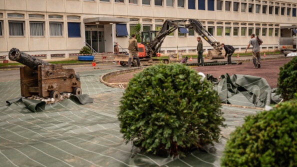 photo d'un grand b&acirc;timent en beton beige, devant lequel manoeuvre un engin de chantier. Des arbustes sont visibles en premier plan.