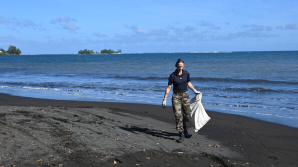 Une gendarme nettoie une plage de sable noir.