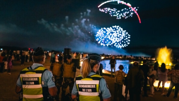 Deux gendarmes de la gendarmerie de l'air devant la foule de nuit. Dans le ciel des feux d'artifice