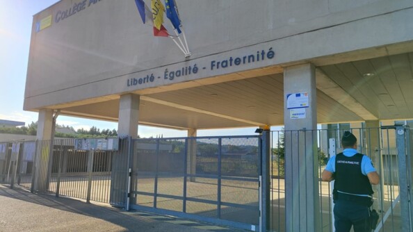 Devant un lycée en béton, à droite, un gendarme devant les grilles