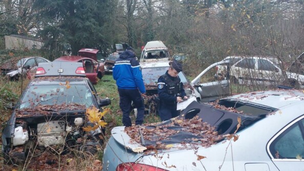 Deux gendarmes relevant les éléments au milieu d'un champ de véhicules épaves