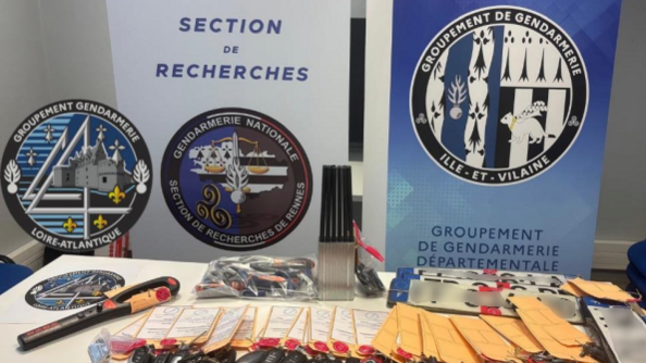Sur une table, de nombreuses clés de voiture sous scellés, des plaques d'immatriculation,  et divers objets sous scellés, sur une table. Derrière la table, deux kakemonos de la Section de recherches de Rennes, du groupement de gendarmerie départementale (GGD) d'Ille-et-Vilaine, ainsi que la rondache du GGD d'Ille-et-Vilaine