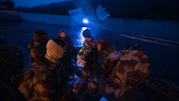 Au premier plan, des miliciens sont en cercles, en train de discuter. En arrière-plan, un quai où est amarré le zodiac de la gendarmerie des voies navigables avec des officiers-élèves autour.