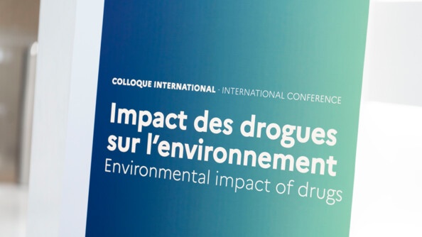 Photo de l'affiche du colloque "Impact des drogues sur l'environnement", dont le titre en lettres blanches apparait sur un fond bleu, se dégradant progressivement vers le vert