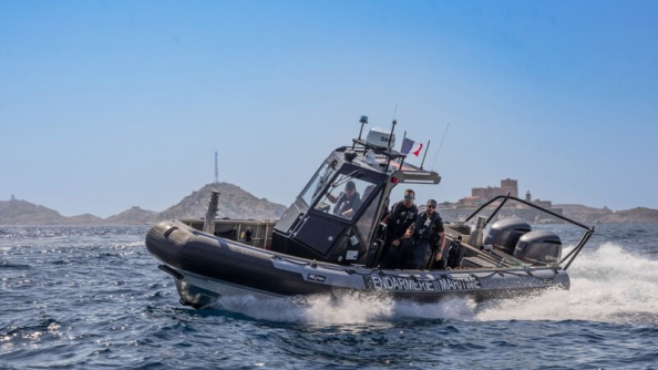 Un zodiac de la gendarmerie nationale évolue en mer. On aperçoit la côte et ses reliefs en arrière plan.