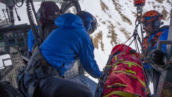 Deux gendarmes dans un hélicoptère en plein vol, en train de prendre en charge une victime dans un brancard qui vient d'être helitreuillé.