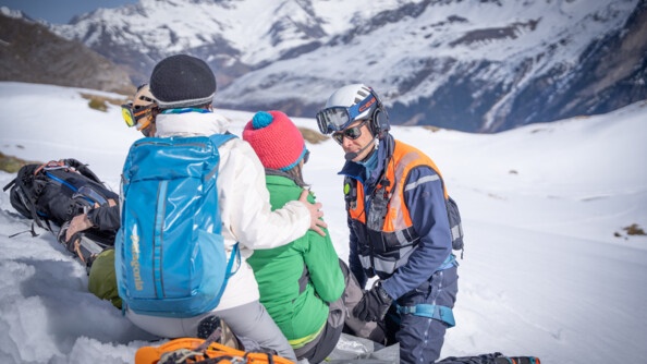 Dans la montagne enneigée, de jour, un gendarme échange avec une femme qui s'est blessé à la jambe.