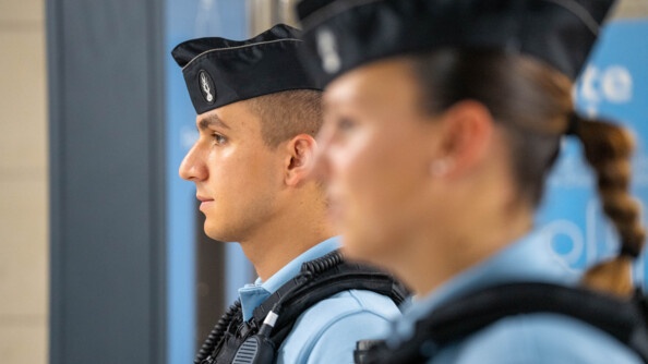 Deux jeunes gendarmes  - un homme et une femme - se tiennent côte à côte, de profil. La femme, située en premier plan, est légèrement floutée.
