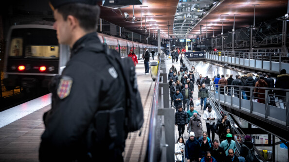 Un gendarme mobile flou au premier plan sur le quai d'une gare RER où il y a de l'affluence