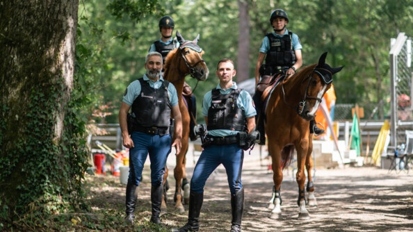 Deux gendarmes debout au premier plan et deux autres à cheval au second plan.