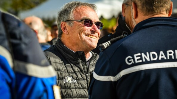 L'ancien coureur cycliste Bernard Hinault échange avec des gendarmes de dos.