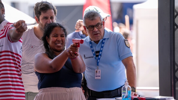 Une femme tire avec un pistolet orange sur un stand de tir. A côté d'elle se tient un gendarme.