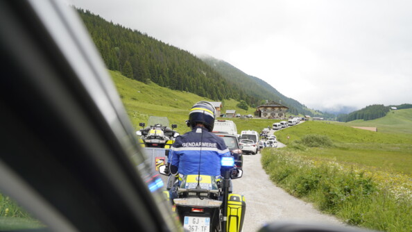 Un motard de la gendarmerie à la fin du cortège de la flamme olympique sur la route traversant un paysage savoyard