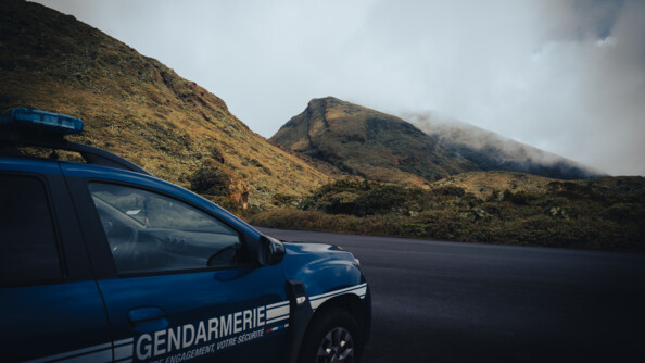 Un Duster sérigraphié gendarmerie, vu trois quart arrière droit, devant un paysage de colline et d'herbe, le tout recouvert par la brume