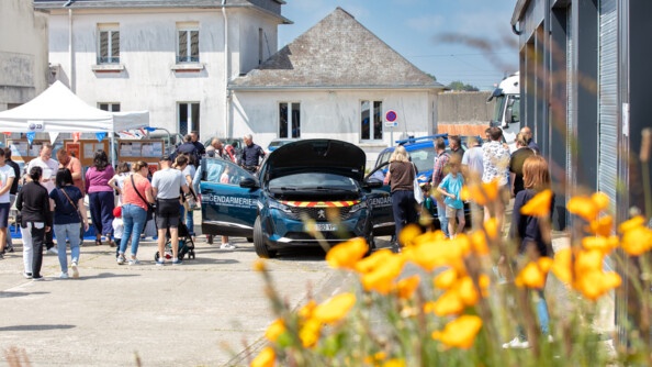 Une voiture de la gendarmerie visitée par le public, derrière des fleurs jaunes au premier plan, floues.