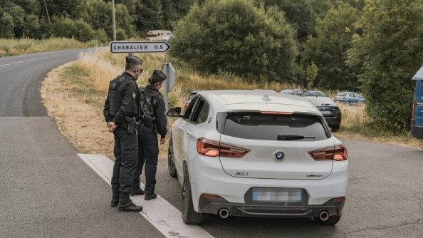 Deux gendarmes, debout, de dos, contr&ocirc;lent un v&eacute;hicule blanc de marque BNW sur une route de campagne