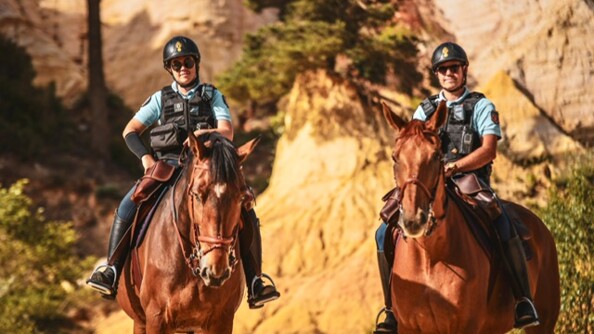 Deux cavaliers gendarmerie sur leur monture, face caméra, dans un paysage minéral de couleur ocre (Rustrel - Vauclause).