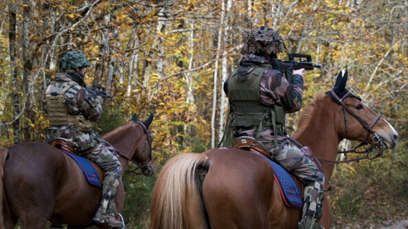 Deux cavaliers de la Garde vus de dos, en treillis, casque sur la tête, sur leur monture, au milieu des bois, vise devant eux avec leur Famas.