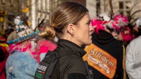 Photo d'une femme gendarme, debout, au milieu de carnavaleux, lors du carnaval de Bergues
