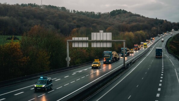 Photo du convoi, ouvert par une voiture de gendarmerie et circulant sur l'autoroute. Il fait jour.