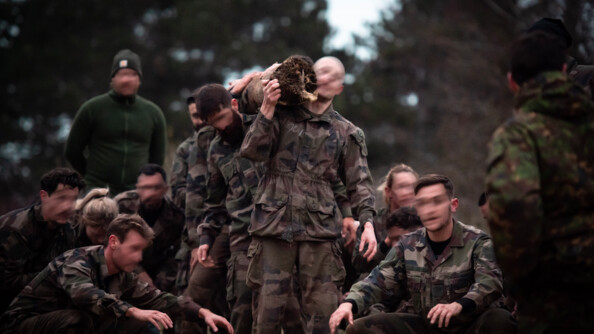 En extérieur, plus de trois militaires portent un tronc de bois. Autour d'eux, d'autres gendarmes sont accroupis