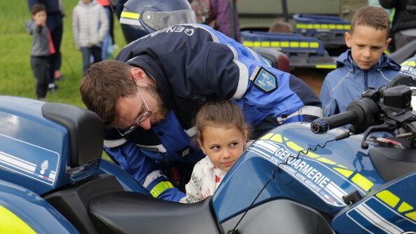 Un gendarme aide une petite fille à monter sur une moto gendarmerie