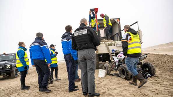 Photo des trois membres du CESAN ainsi que cinq membres de l'organisation de l'événement. Sur le côté droit un quad avec une fuite d'essence est posé sur un tapis qui absorbe le liquide afin de ne pas polluer les sols. Ils sont entrain de prendre le quad pour le mettre dans un camion.