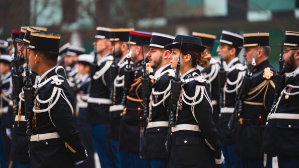 Une gendarme en uniforme se tient debout, de biais, au milieu d'hommes, gendarmes eux-aussi.