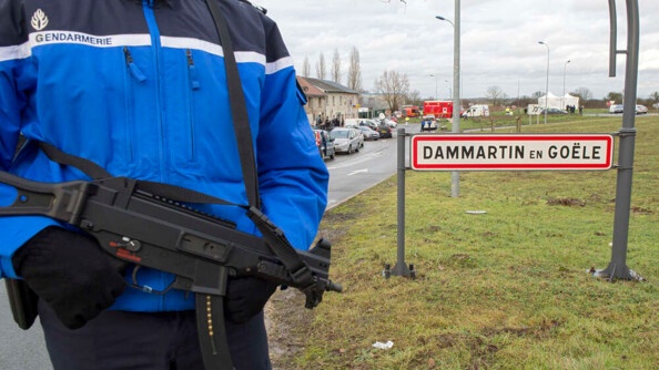 Au premier plan, un gendarme en tenue d'intervention, portant un blouson d'hiver et des gants, avec un Famas en bandoulière. On ne voit pas sa tête. Il est debout à l'entrée d'un village. Derrière lui la pancarte DAMMARTIN EN GOELE.